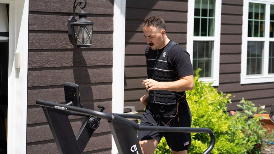 A man running outside on a treadmill, while testing the Hyperwear Hyper Vest Elite Weight Vest in black.